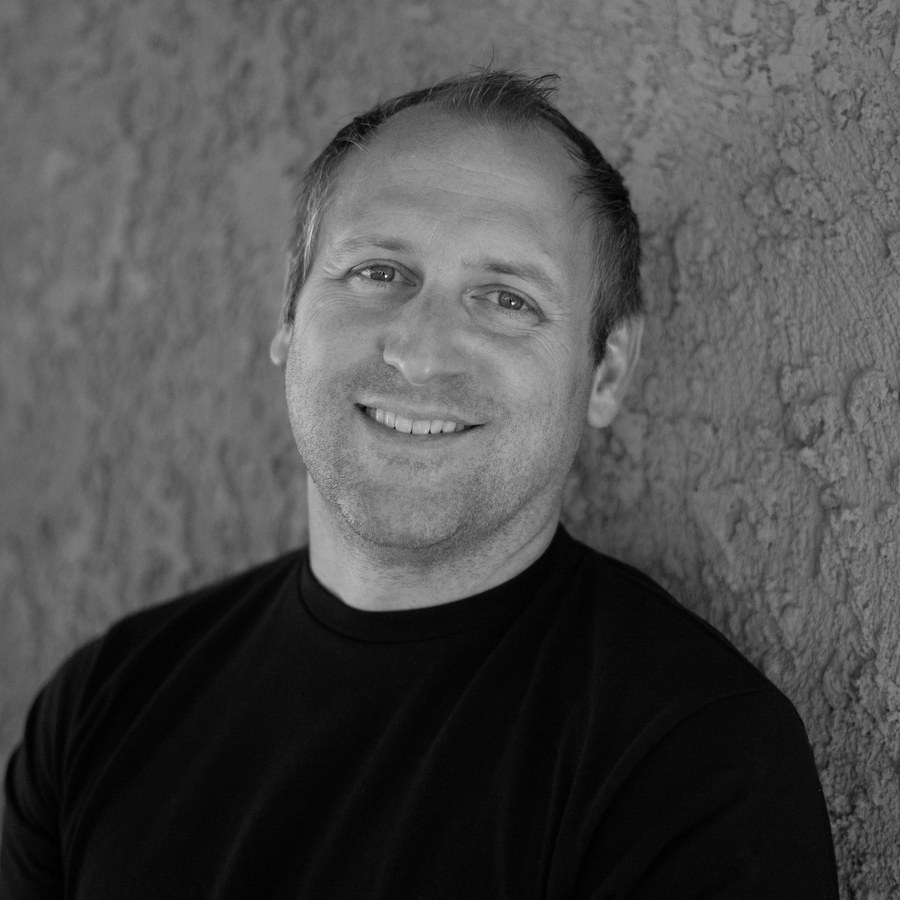 Dave, in black and white, smiling against a stucco wall.